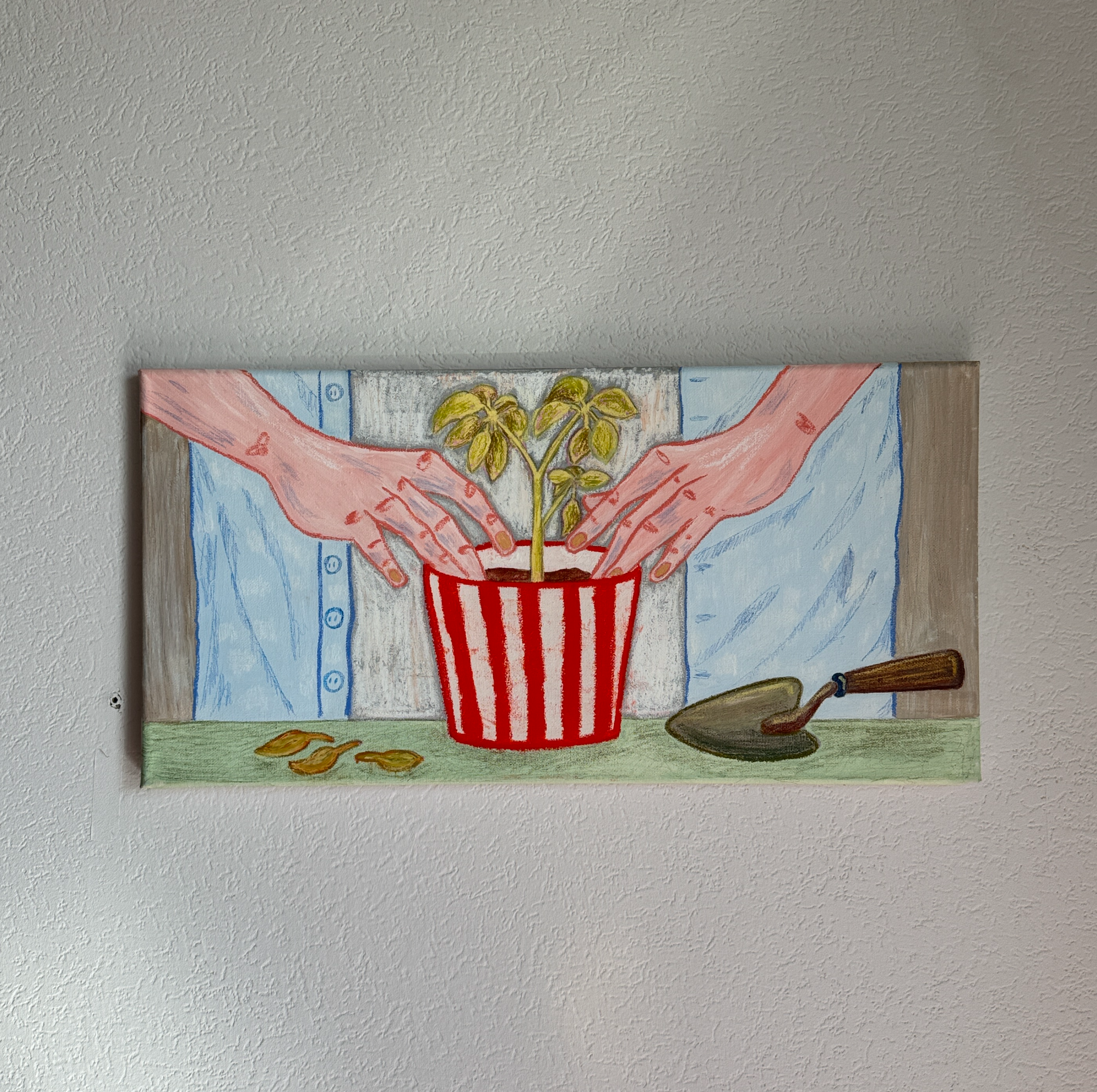 Картина, выполненная гуашью, масляной пастелью и карандашами на холсте, висит на светлой стене и изображает две руки в голубой рубашке, сажающие зеленый росток в полосатый горшок, рядом лежат совок и несколько коричневых листьев