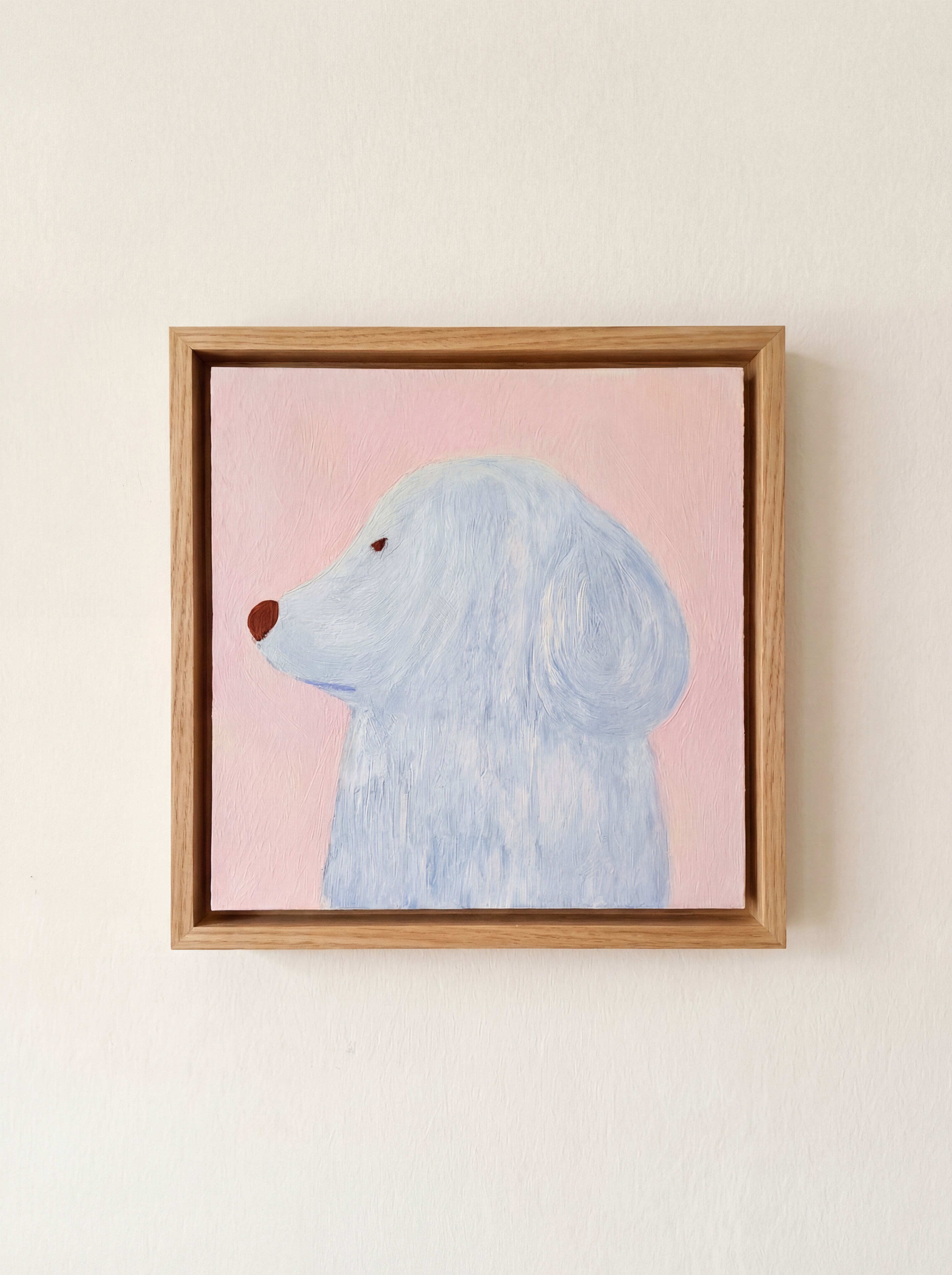 Картина маслом на бумаге с изображением головы и части туловища светло-голубой собаки в профиль на розовом фоне в светлой деревянной раме висит на белой стене, бумага